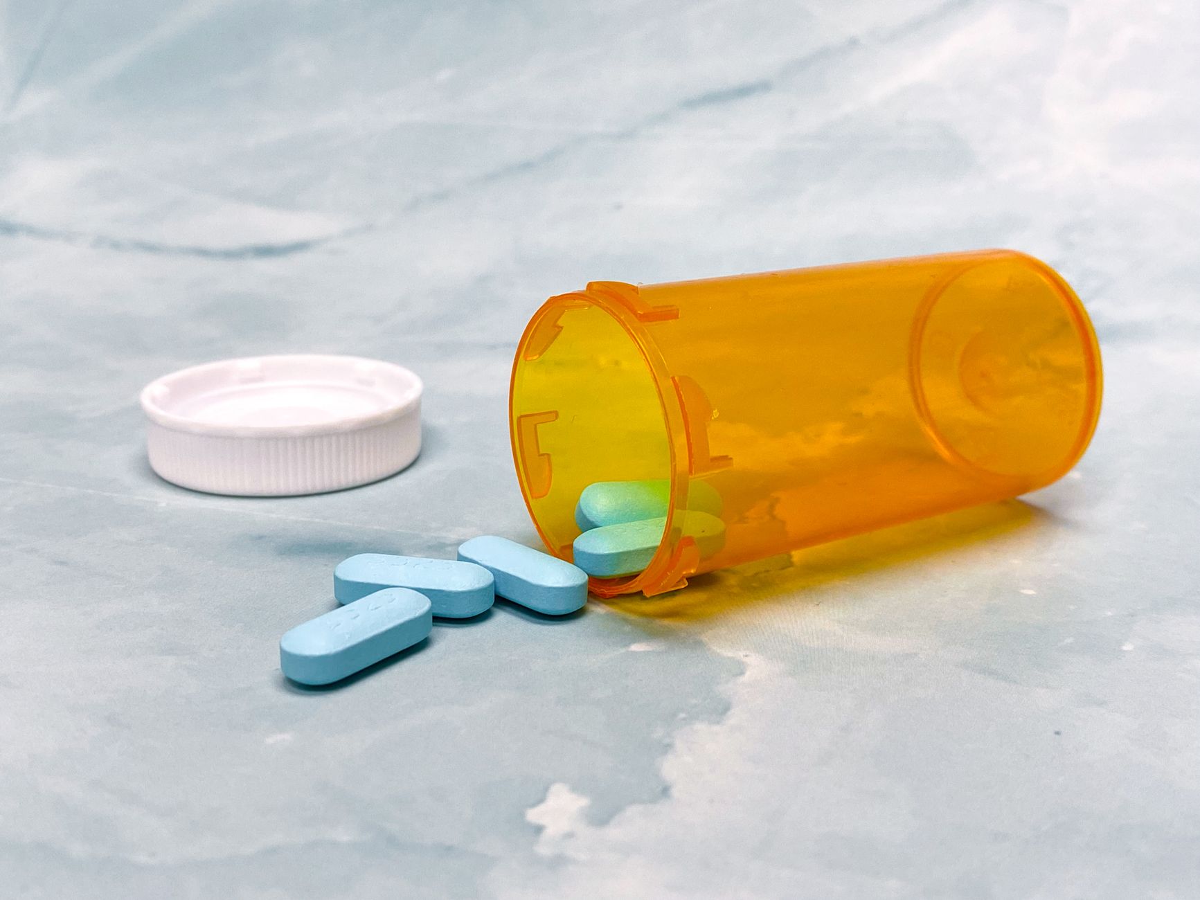 an orange prescription bottle tipped over with blue tablets spilling out